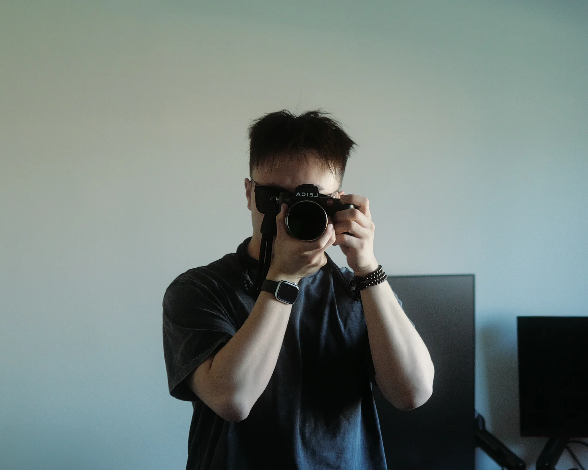 Mirror portrait holding a Leica camera in a softly lit room