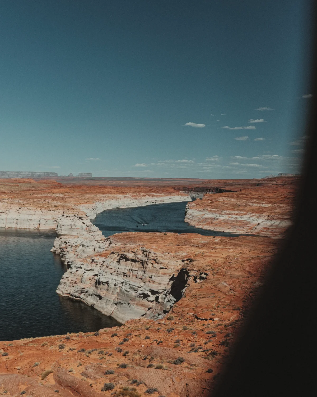 A boat crossing blue water between pale cliffs and rust-colored desert rock