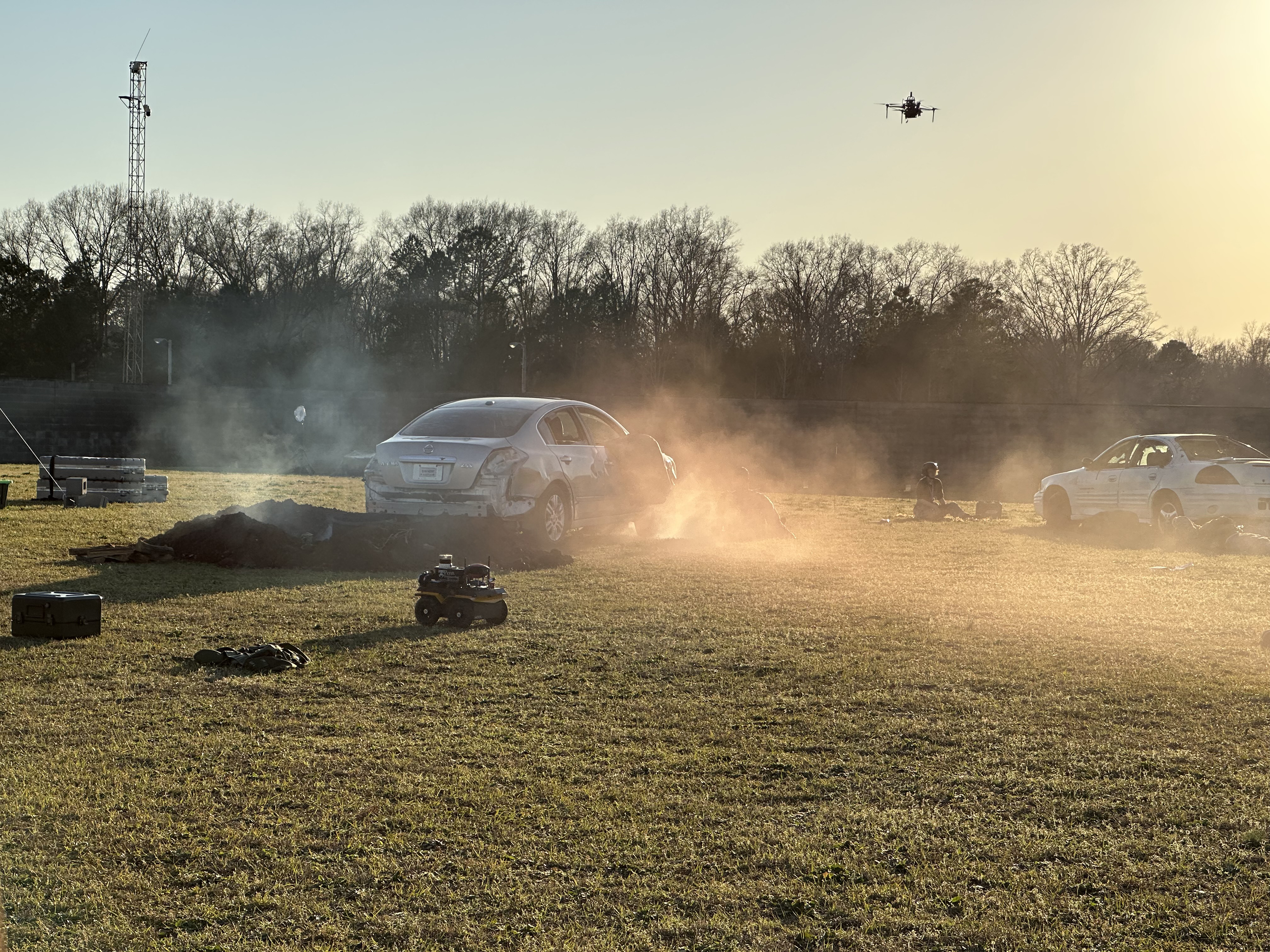 A ground robot and airborne drone at an outdoor triage exercise with vehicles and simulated casualties